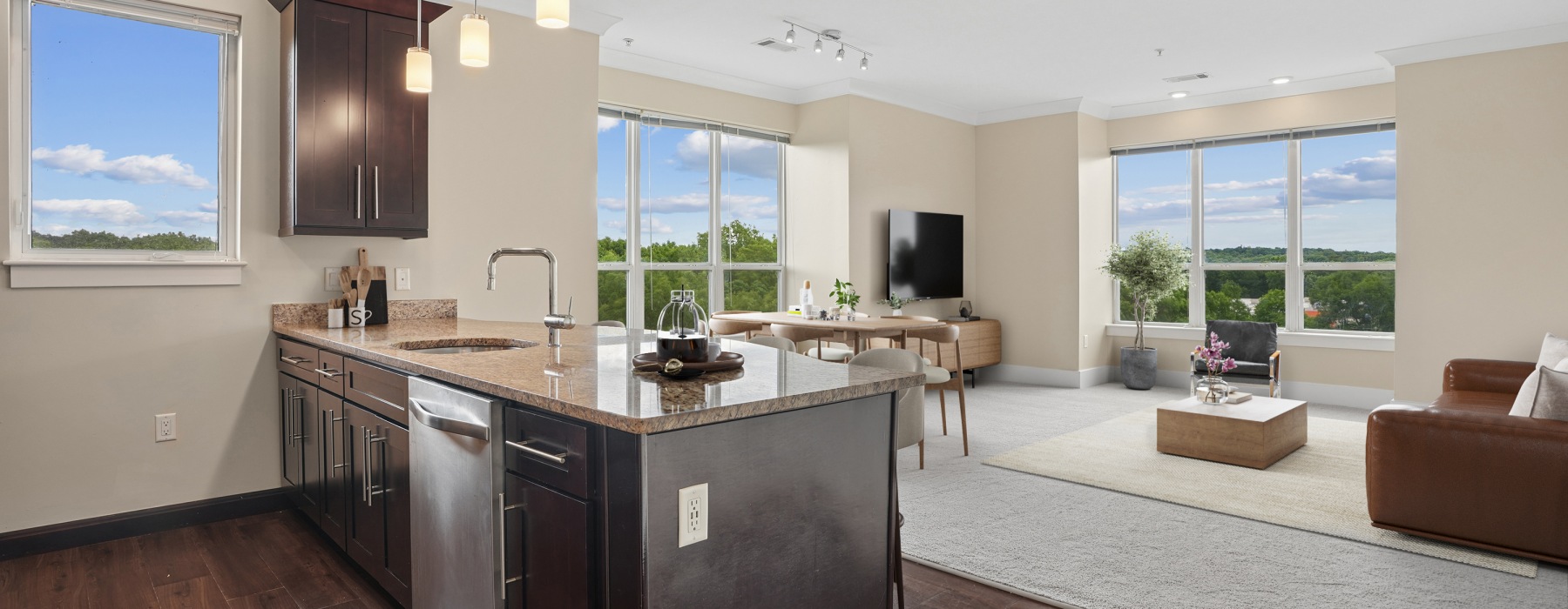Wide banner view of a modern apartment interior at Matrix Hudson showcasing a contemporary kitchen island and a bright, open living room layout in Hudson, MA.